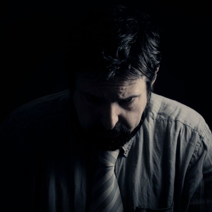 Hombre con barba, camisa y corbata con la cabeza gacha, la imagen es muy oscura